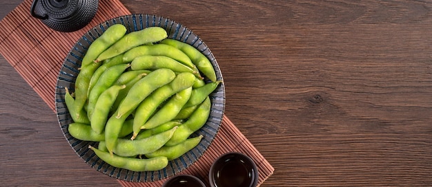 Fresh cooked boiled edamame in a plate on wooden tray and table background healthy protein food concept