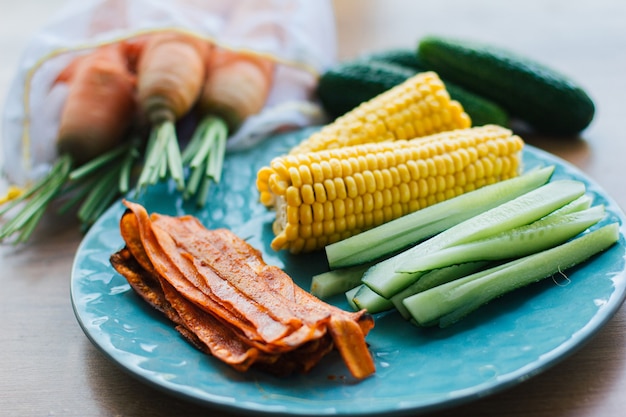 Fresh cooked carrot bacon lies on a turquoise plate with corn and cucumber. Vegetarian food, meat replacement, protein, healthy snack