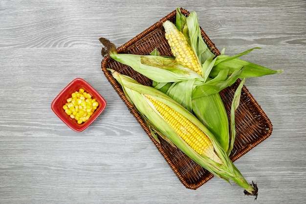 Fresh corn cob in esparto halfah basket and bowl on wood table