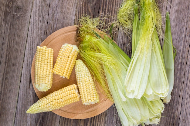 Свежая кукуруза на початках на деревенском деревянном столе, крупном плане, вид сверху, космос экземпляра.