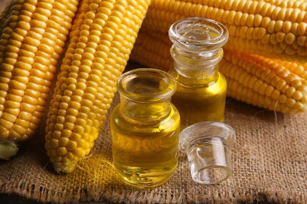 Photo fresh corn with bottles of oil on table close up