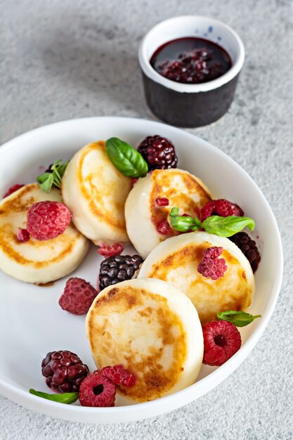 Foto frittelle di ricotta fresca o frittelle di ricotta syrnikifritters su un piatto bianco con frutti di bosco freschi e marmellata colazione deliziosa e sana di ricotta cucina russa ucraina cibo dolce