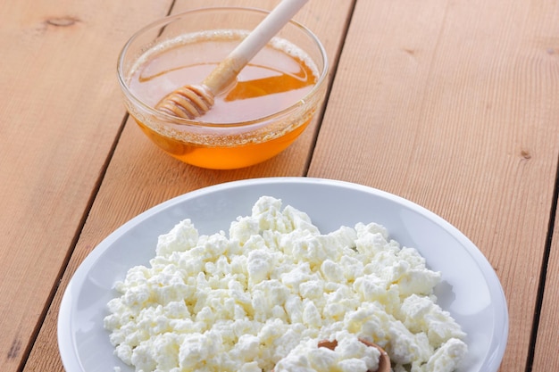 白い皿に新鮮なカッテージ チーズ木の背景にカッテージ チーズと蜂蜜木のスプーンに入ったサワー クリーム乳製品のコンセプト