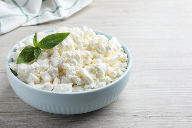 Fresh cottage cheese with basil in bowl on light wooden table