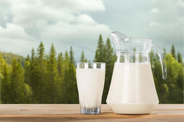 Fresh cow milk in glass and jug on wooden table