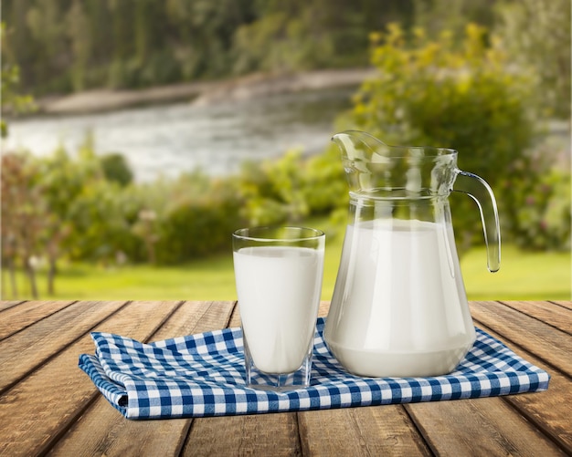 Свежее коровье молоко в стакане и кувшине на деревянном столе