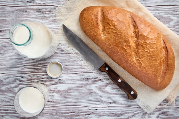 Fresh cow's milk and a loaf of white, warm, soft bread on a wooden table, top view