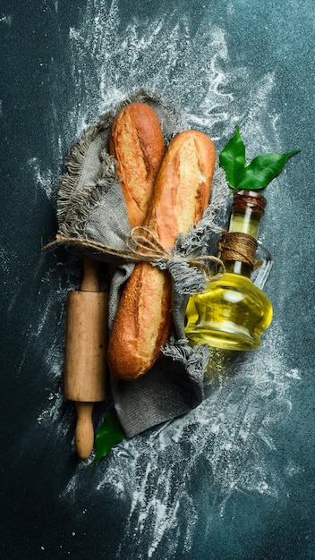 Fresh crispy baguette a jar of oil and a rolling pin on a dark background Free space for text