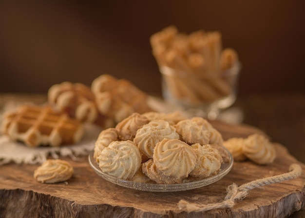 Fresh crispy shortbread cookies on a glass plate against the background of viennese waffles on a wooden tray light brown background