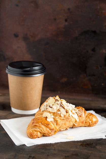 Photo fresh croissant and coffee in a paper cup on dark