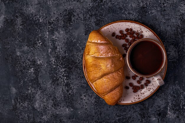 Fresh croissant on dark surface with coffee