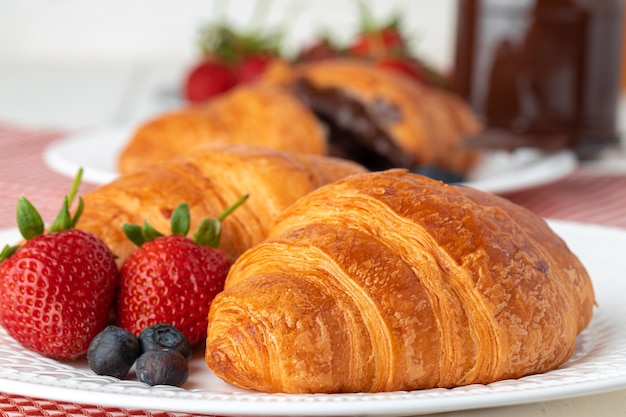 Fresh croissant decorated with berries on white wooden board close up