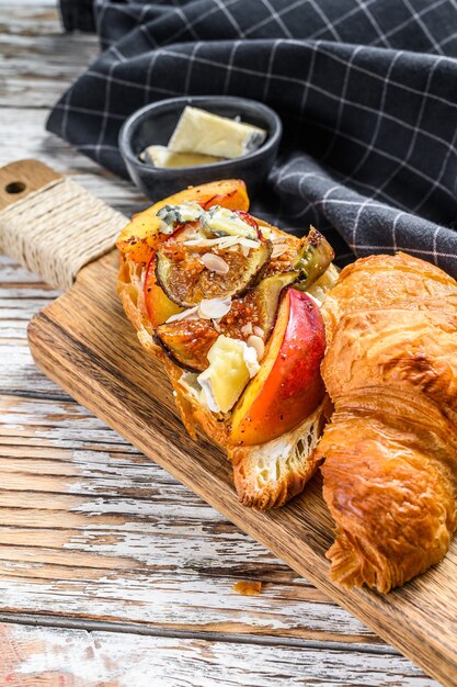 Fresh croissant sandwich with brie cheese, peach and figs. Delicious breakfast. White background. Top view.