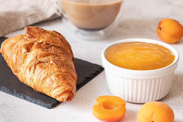 Fresh croissant, served with apricot jam and coffee. French breakfast concept, grey background