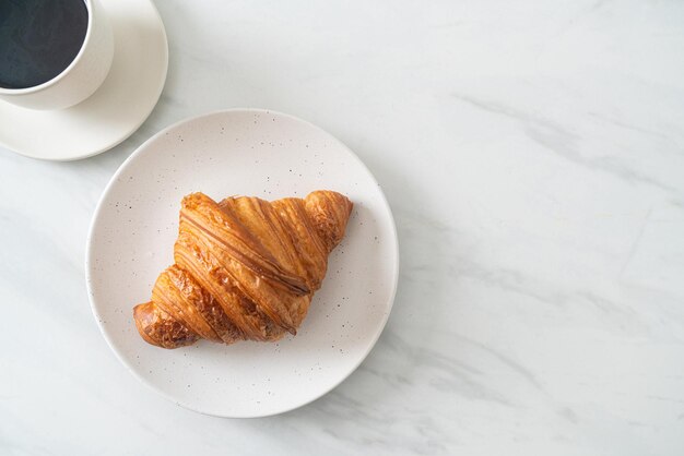 Croissant fresco sul piatto bianco con caffè nero