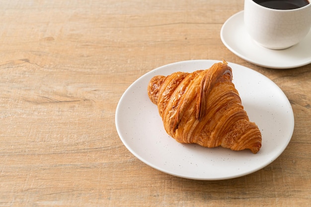 Fresh croissant on white plate with black coffee