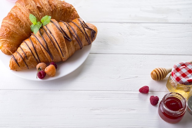 Fresh Croissant with berries and jam for breakfast isolated on white wooden background 