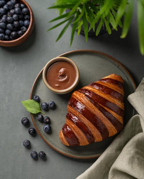 新鮮なクロワッサン チョコレートとブルーベリーで 緑色の背景に 黒い皿に 枝で 美味しい自家製の朝食コンセプト 田舎風