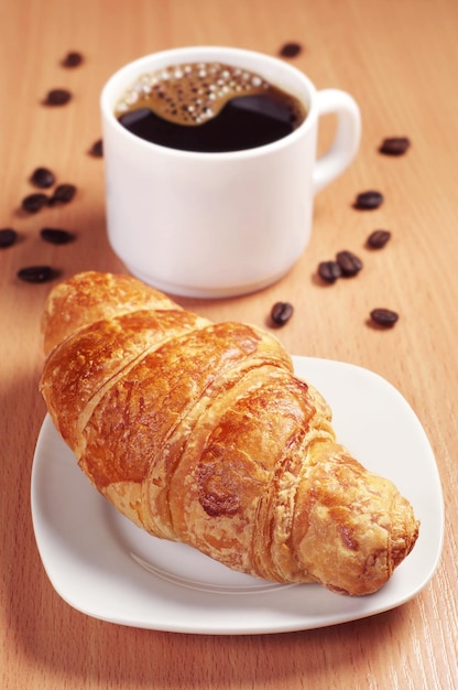 Fresh croissant with cup of hot coffee on desk