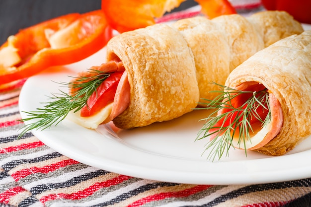 Fresh croissant with ham and salad leaf on dark wooden background