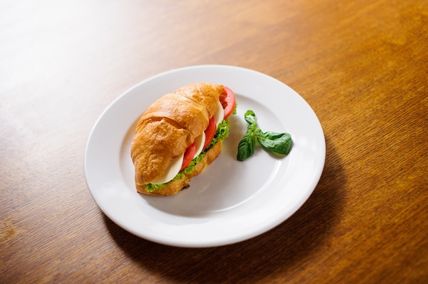 Fresh croissant with ham and salad leaf on dark wooden background