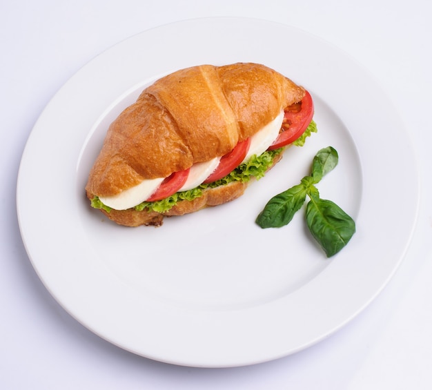 Fresh croissant with ham and salad leaf on grey background