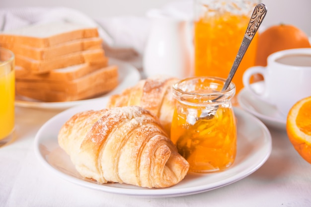 Fresh croissants buns, oranges, orange jam. Breakfast concept.