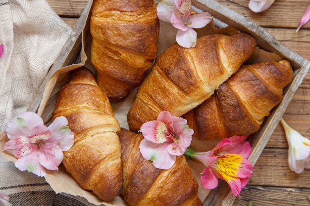 Fresh croissants and flowers in a tray on a wooden table top view