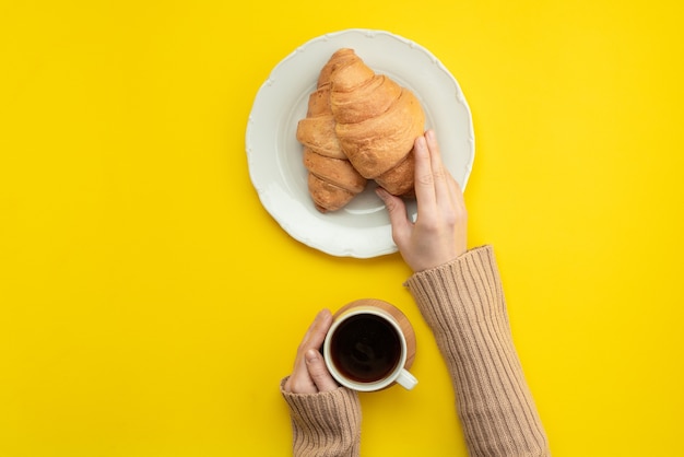 Fresh croissants and hot coffee, a female hand holding a cup