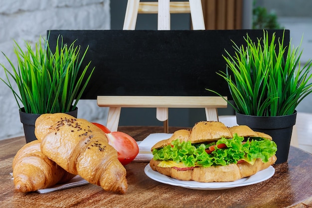 Fresh croissants with pork chicken tomatoes cucumbers salad on a white plate on a wooden table.