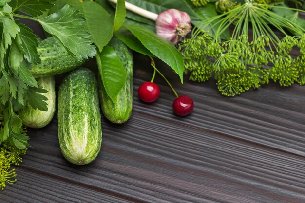 Fresh cucumbers and cherries among dill and parsley. Head of garlic. Wooden background. Top view. Copy space