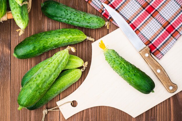 Fresh cucumbers on the cutting board and knife on a wooden table. Top view