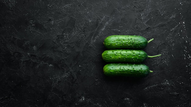 Fresh cucumbers with green leaves on a black background. Top view. Free space for your text.