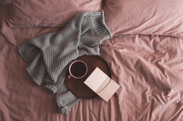 Fresh cup of coffee or black tea with open sketch book and knitted sweater in bed closeup. Good morning. Breakfast time.