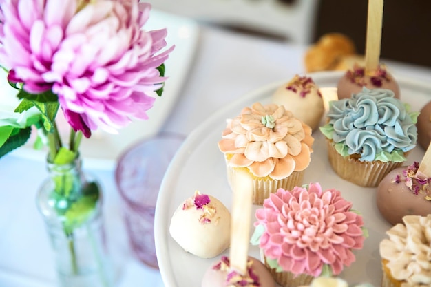 Fresh cupcakes with whipped cream and devorative flower icing served on a plate on party table weddi