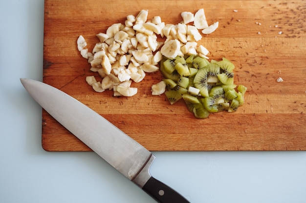 Fresh cut of banana and kiwi on wooden chopping board with knife isolated on white from above flat lay