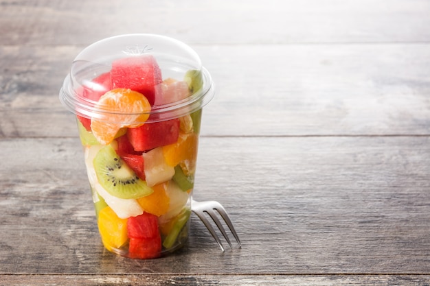 Fresh cut fruit in a plastic cup on wooden table