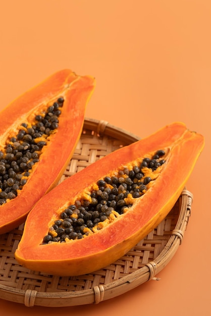 Photo fresh cut papaya fruit over orange table background for tropical gourmet design concept