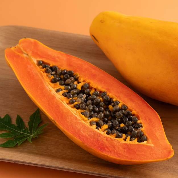 Photo fresh cut papaya fruit over orange table background for tropical gourmet design concept