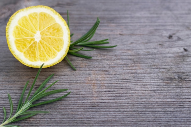 Fresh cuted juicy lemon and green rosemary twigs on the wooden background