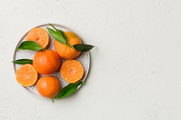 Fresh cutted clementines and whole mandarin over round plate on colored background Food and drink ingredients preparing healthy eating theme top view vith copy space