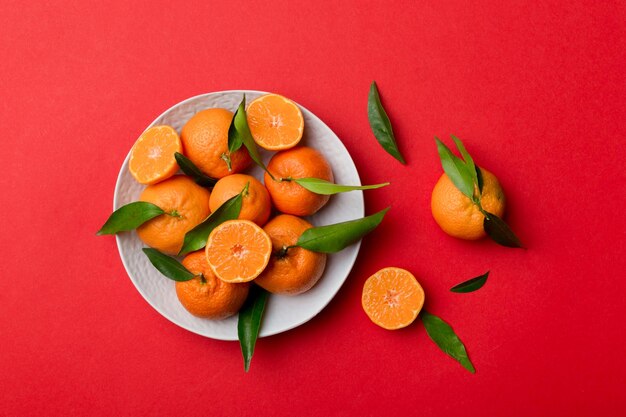 Fresh cutted clementines and whole mandarin over round plate on colored background food and drink ingredients preparing healthy eating theme top view vith copy space