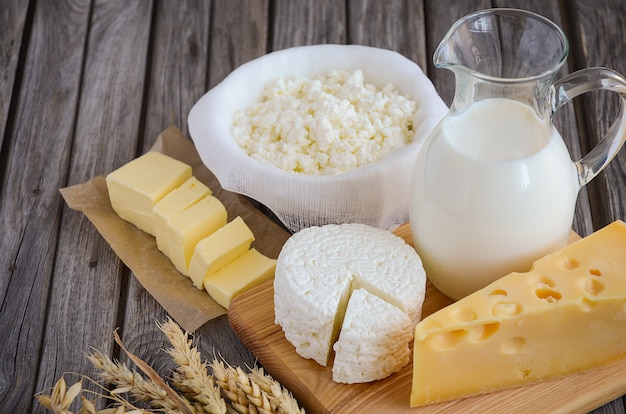 Photo fresh dairy products. milk, cheese, butter and cottage cheese with wheat on the rustic wooden background.