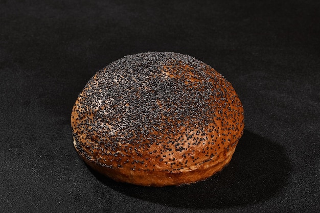 Fresh delicious baked bun sprinkled with poppy seeds against black background with copy space Rural cuisine or bakery Closeup