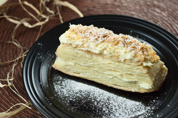 Foto deliziosa torta napoleone fresca con crema, su un nero.