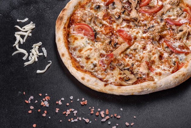 Fresh delicious Italian pizza with mushrooms and tomatoes on a dark concrete background. Italian cuisine