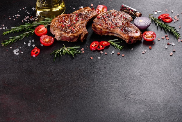 Fresh delicious juicy steak on the bones with vegetables and spices. Pork juicy steak grill on dark table