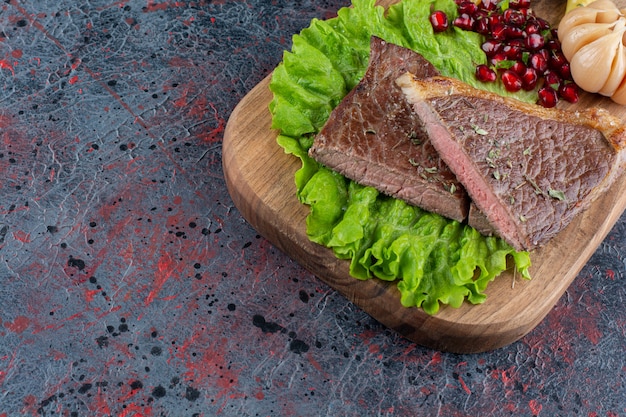 Fresh delicious juicy steak with lettuce salad placed on wooden cutting board.