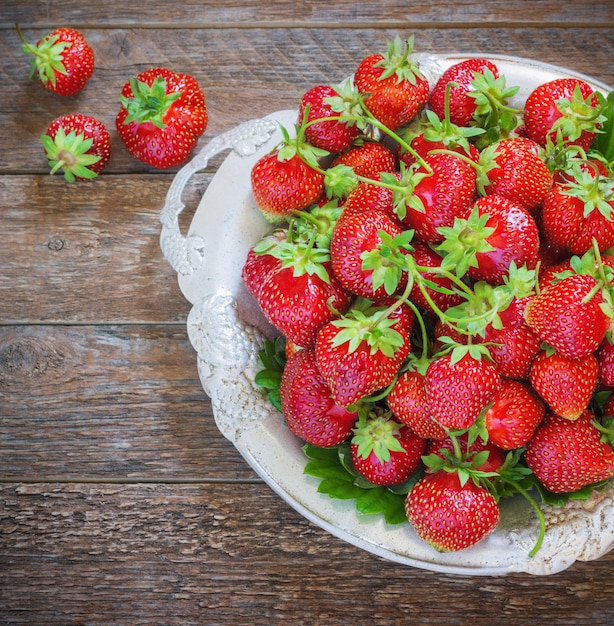 Fresh and delicious organic strawberries on old metal plate, wooden table. Perfect for your healthy eating dieting.