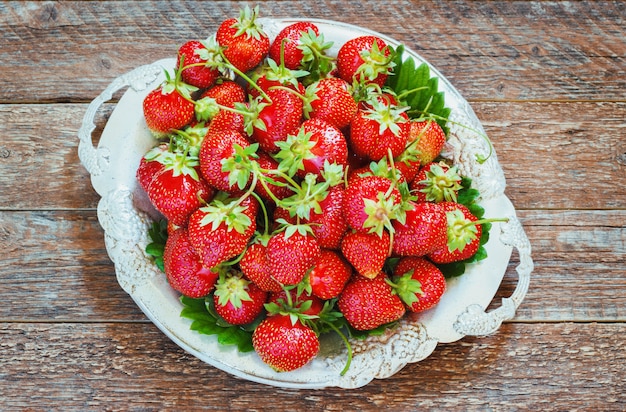Fresh and delicious organic strawberries on old metal plate, wooden table.